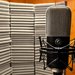 **

Close-up studio shot of a condenser microphone with a pop filter, positioned in front of a sound-treated vocal booth. The focus should be on the microphone capsule. Soft, diffused lighting. The background shows acoustic foam panels and bass traps. Aim for a professional and inviting atmosphere, emphasizing clarity and audio quality.

**